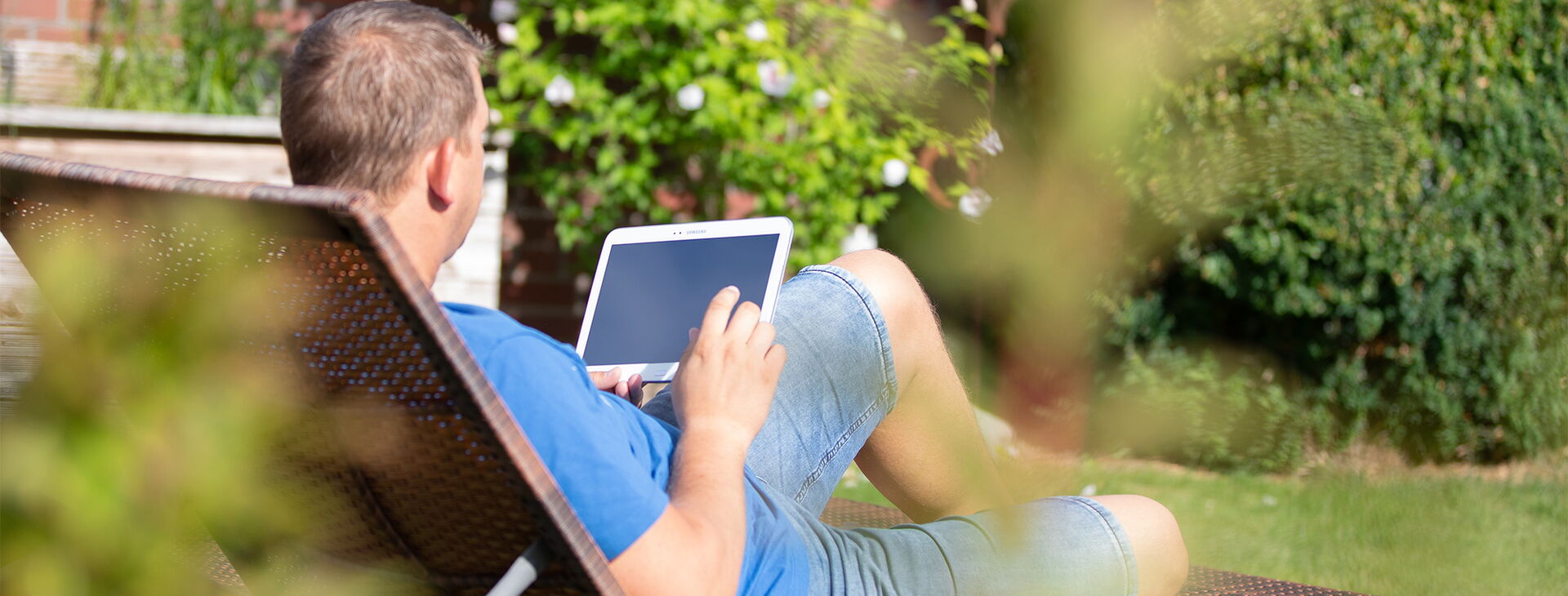 Ein Mann der draußen auf einer Liege liegt und ein Tablet in der Hand hält