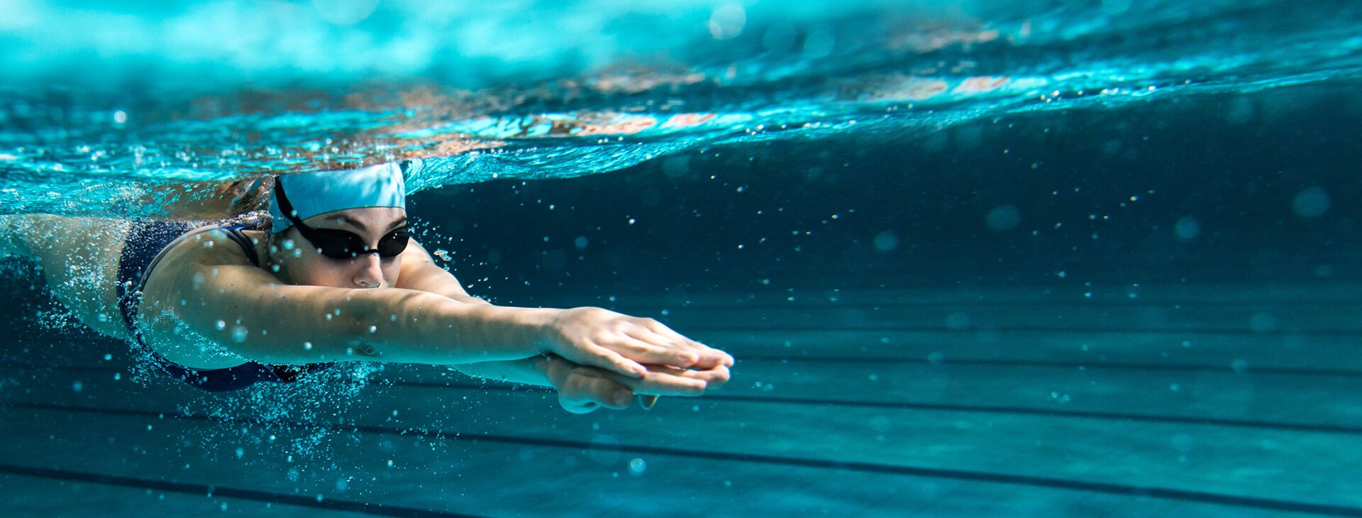 Schwimmerin mit Taucherbrille und Haube gleitet unter Wasser