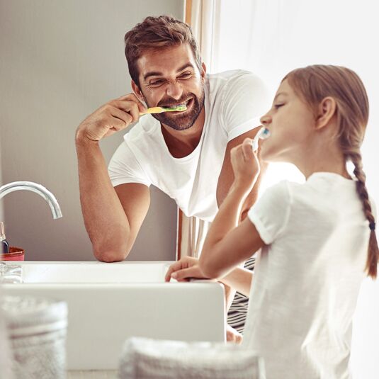 Vater und Tochter putzen ihre Zähne und schneiden Grimassen