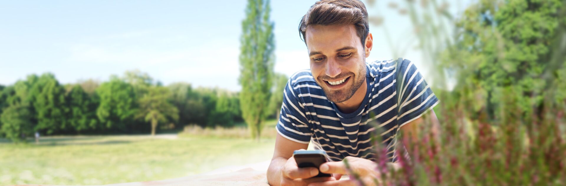 Ein glücklicher Mann, auf einer Wiese liegend und mit eine Smartphone in der Hand