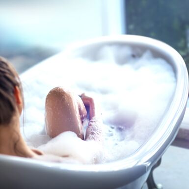 Eine Frau sitzt in einer warmen schaumigen Badewanne und guckt aus dem Fenster
