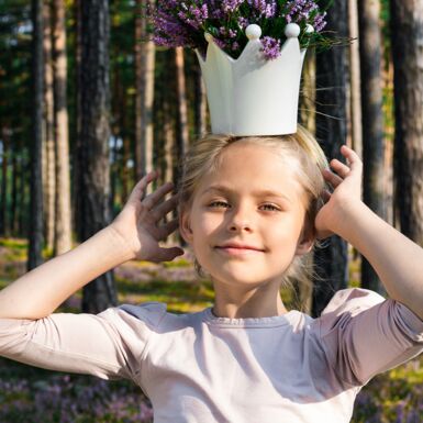 Ein Mädchen im Wald mit einer Krone in der sich Heideblumen befinden auf dem Kopf