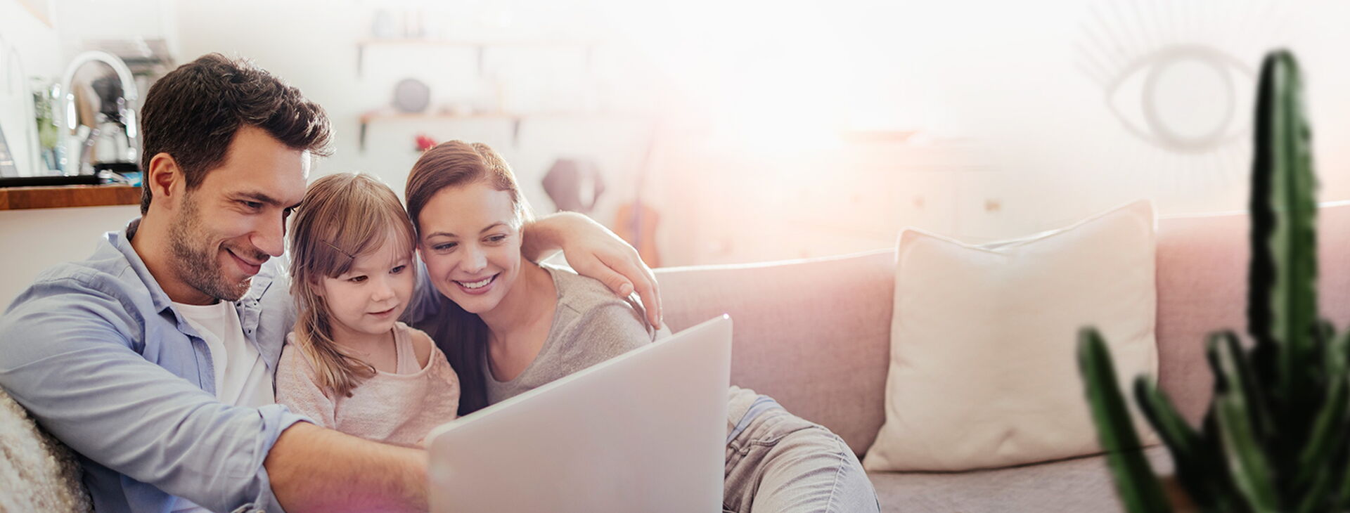 Mutter, Vater und Tochter liegen auf dem Sofa und schauen sich etwas auf dem Laptop an