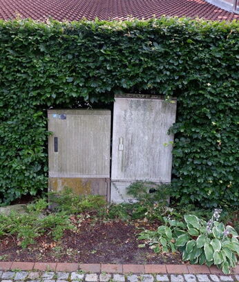 Zwei Kabelverteiler-Schränke die in einer Hecke stehen