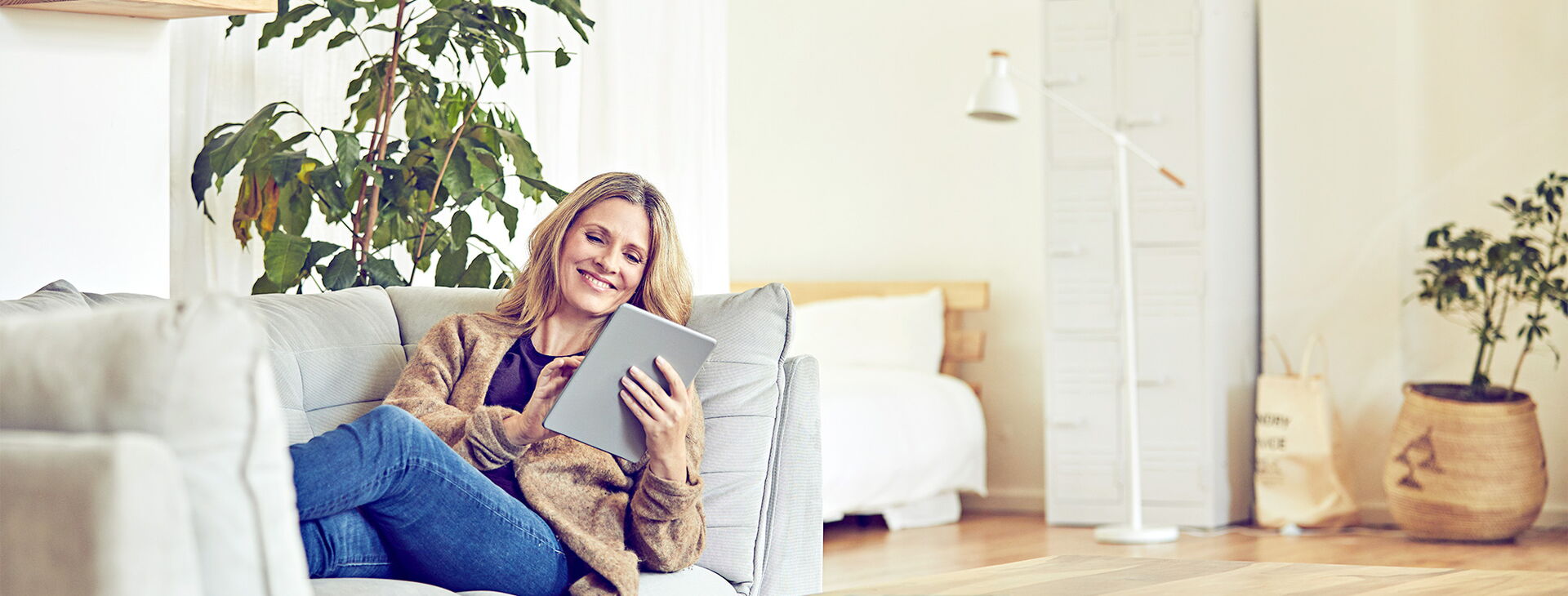 Eine glückliche Frau die auf dem Sofa liegt und ein Tablet in der Hand hält