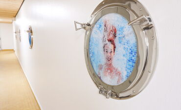 Ein Bullauge als Bilderrahmen, im Bild ist eine Frau unter Wasser zu sehen. Das Bild hängt in einem Flur im Heidjers Wohl.